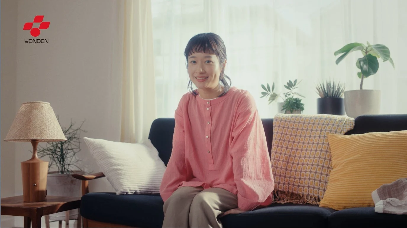 明るいリビングのソファに座り、笑顔を見せる女性の姿