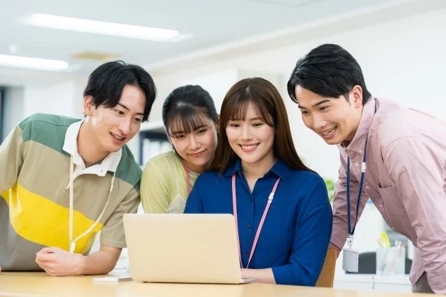 4人の男女がノートパソコンを囲んで笑顔で画面を見つめている画像