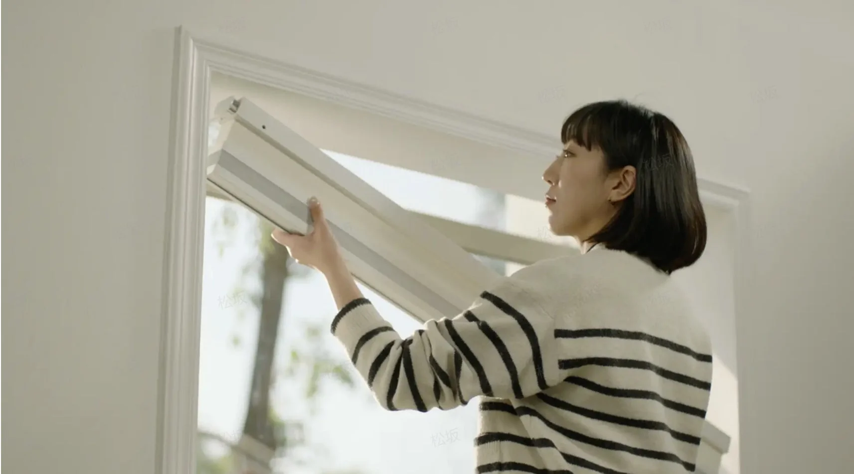 女性が窓にブラインドを取り付けている様子