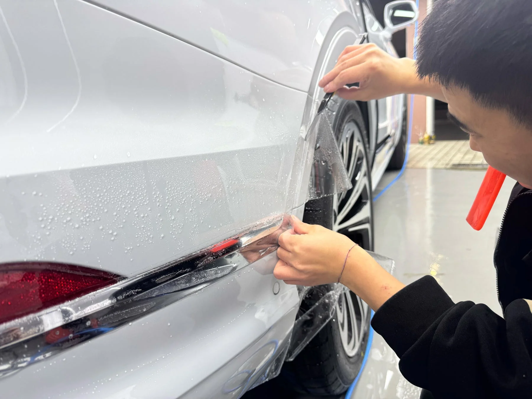 白い車の後部フェンダーにプロテクションフィルムを施工している様子