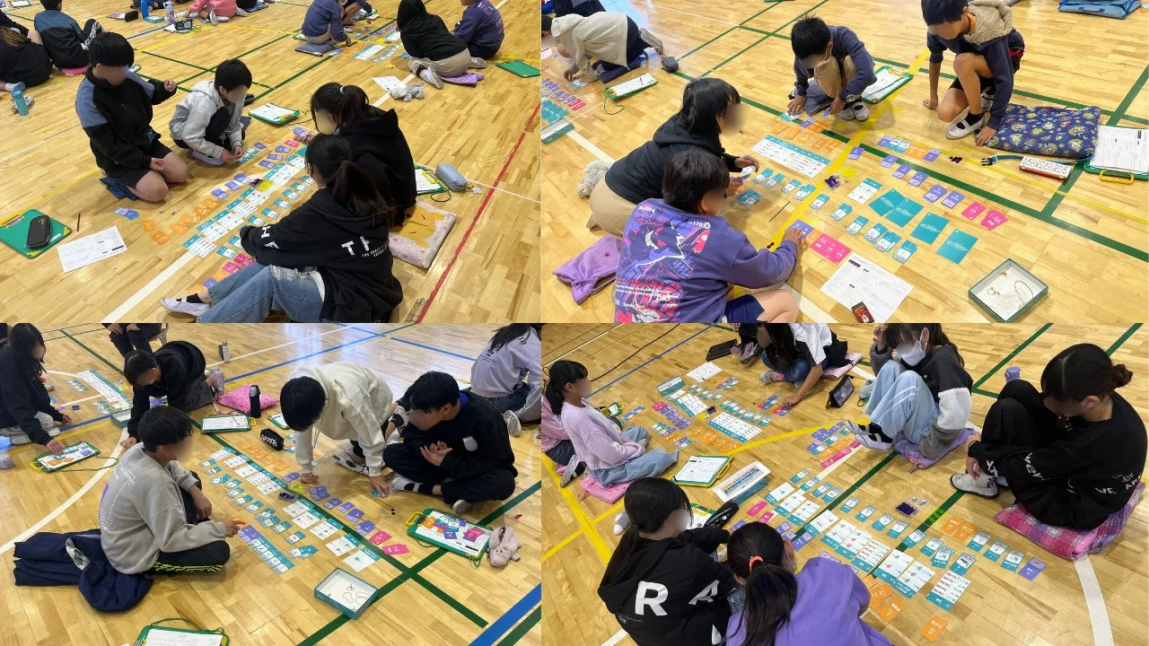 子供たちが床に座り、カラフルなカードを並べて学習活動に取り組んでいる様子