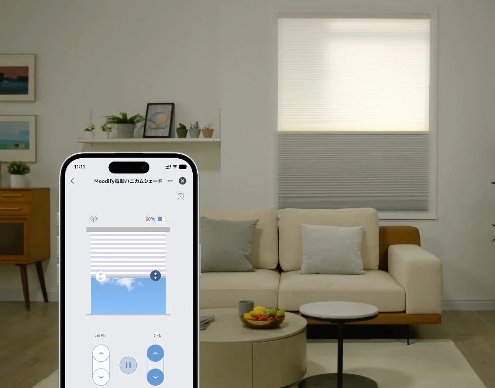 モダンなリビングルームで、スマートフォンアプリを使って電動ハニカムシェードを操作している様子