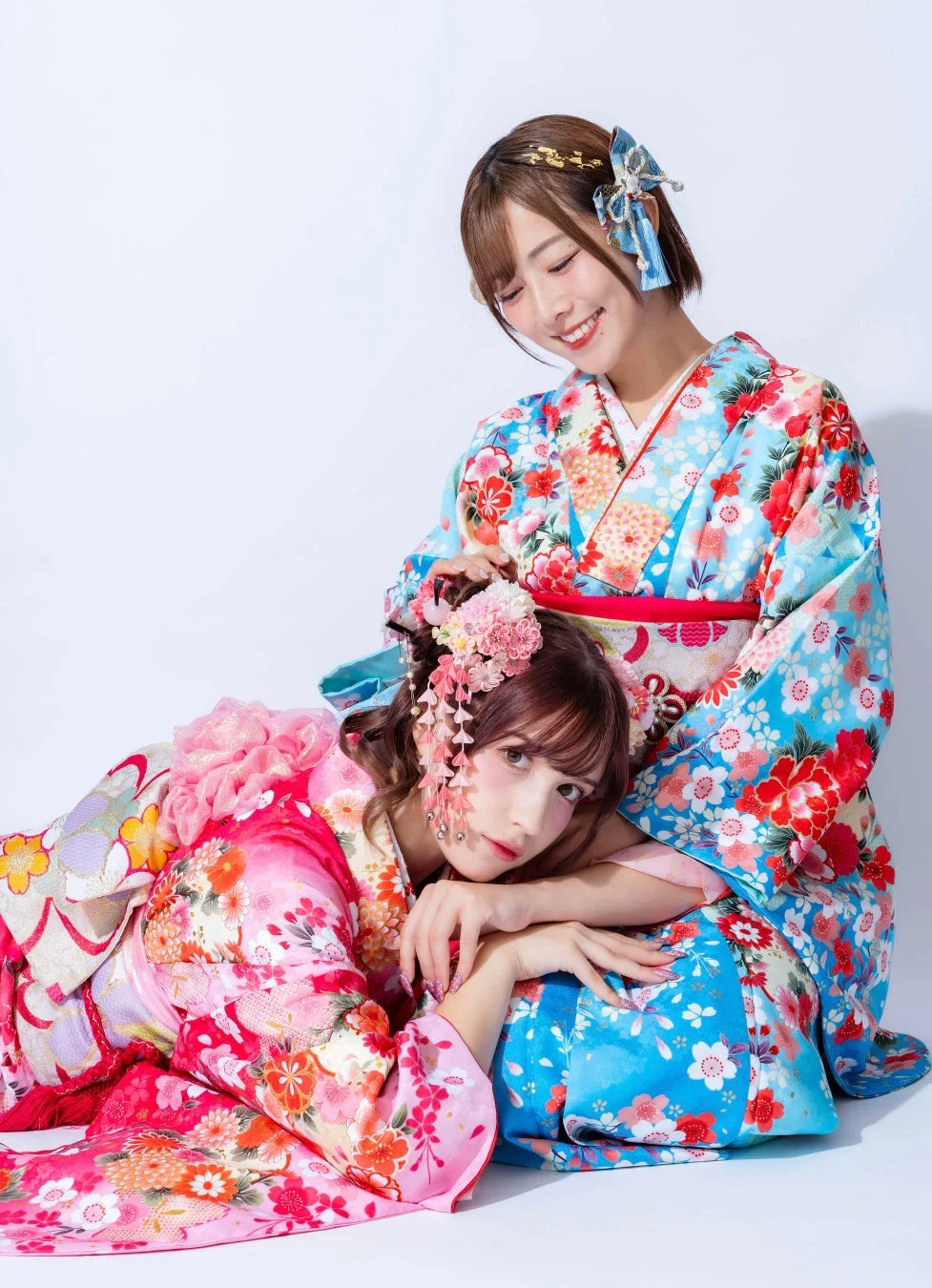 鮮やかな花柄の着物をまとった二人の女性が、笑顔で寄り添い合うポートレート。華やかな髪飾りをつけ、日本の伝統美を感じさせる一枚です。