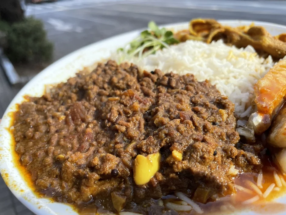 屋外で提供されているキーマカレーのプレートです。白いご飯と、ひき肉を使った濃厚なカレー、そして付け合わせと思われるサイドディッシュが盛り付けられています。