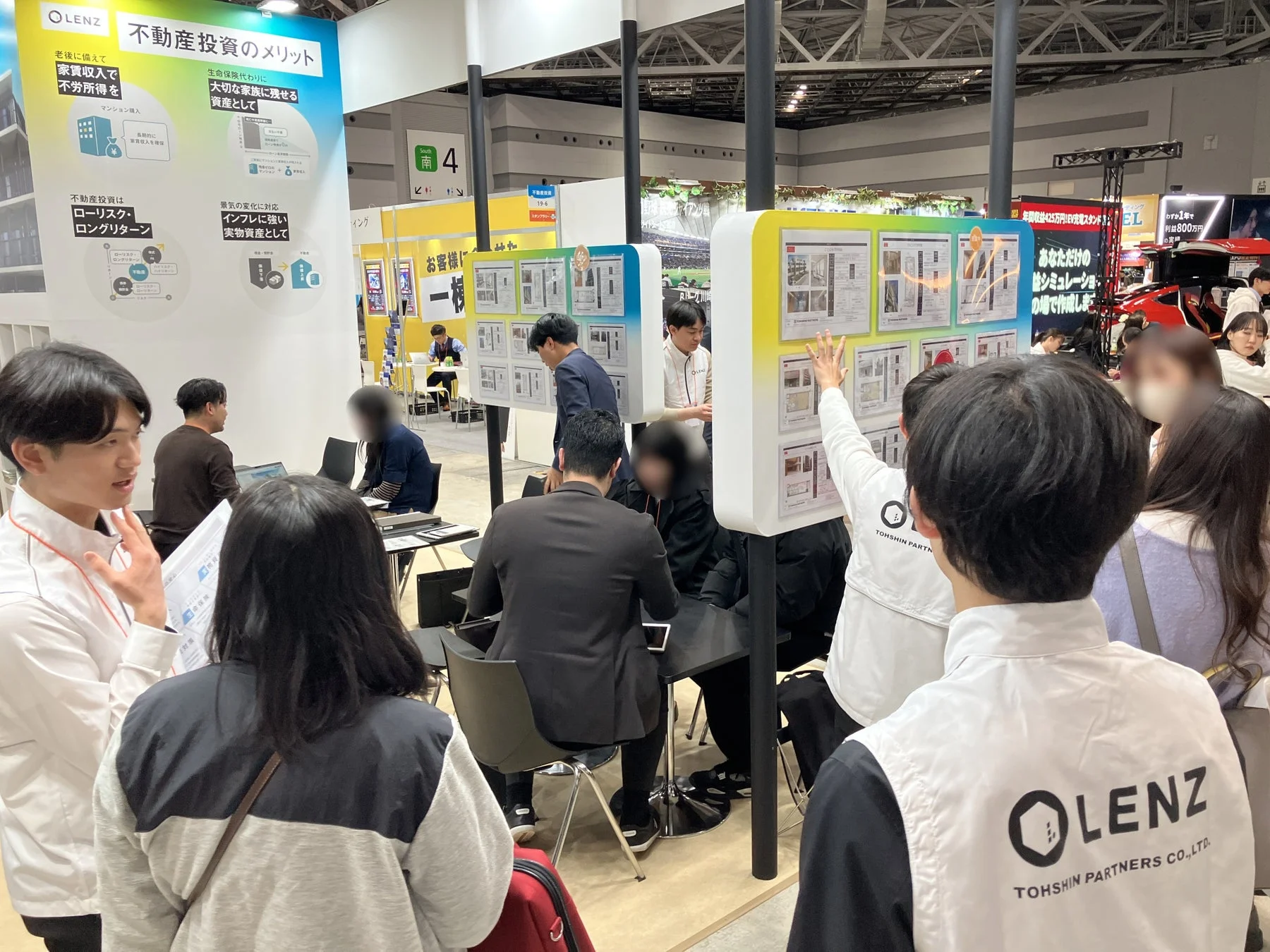 展示会の不動産投資ブースで、多くの来場者がスタッフから投資メリットやシミュレーションの説明を受けている様子