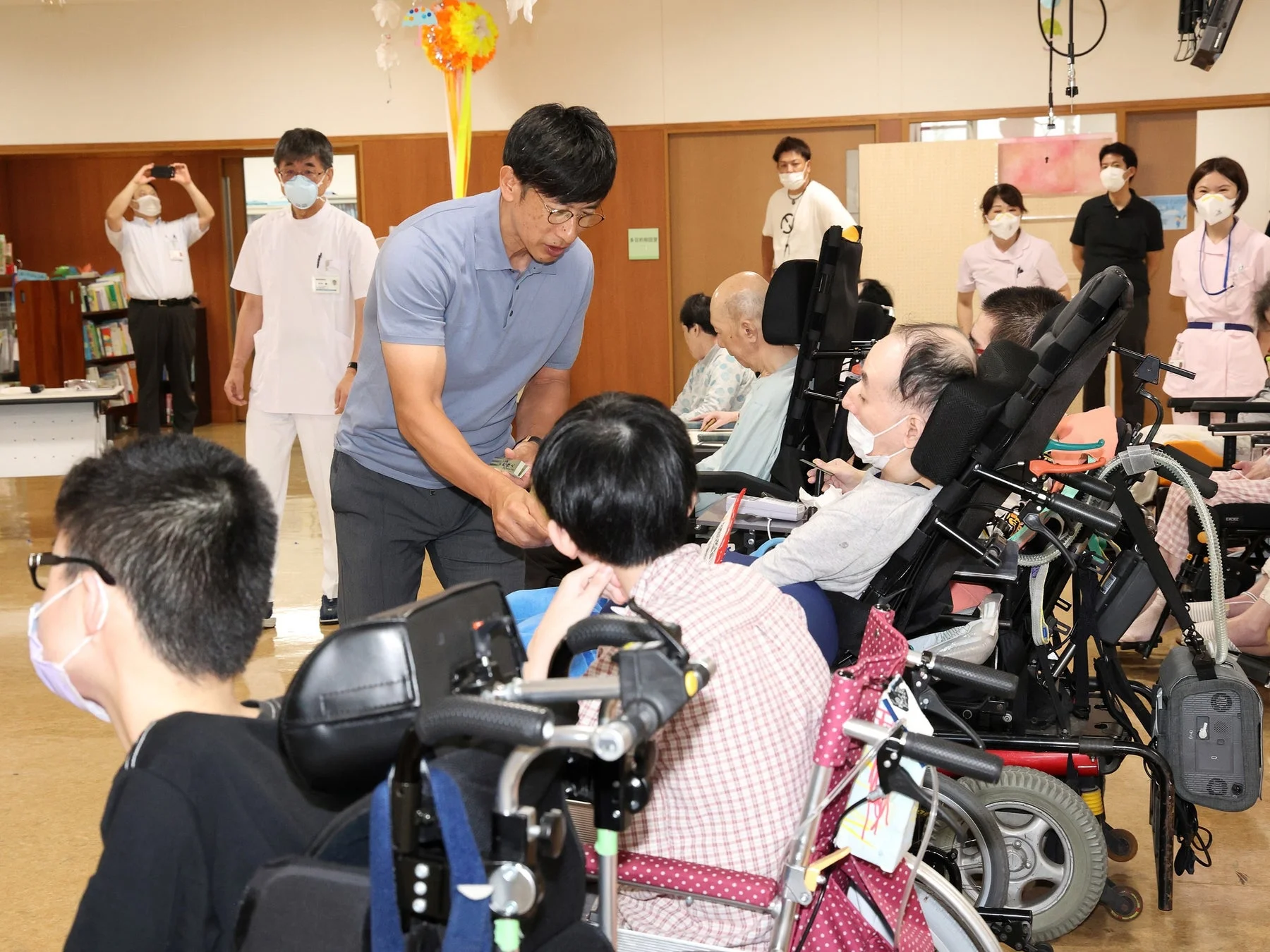 介護施設と思われる屋内で、男性が車椅子の利用者に話しかけている様子