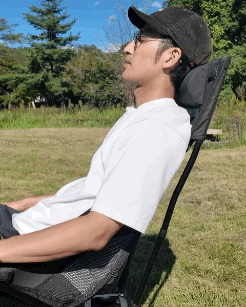 屋外で折りたたみ椅子に座り、リラックスして空を見上げている男性の横顔