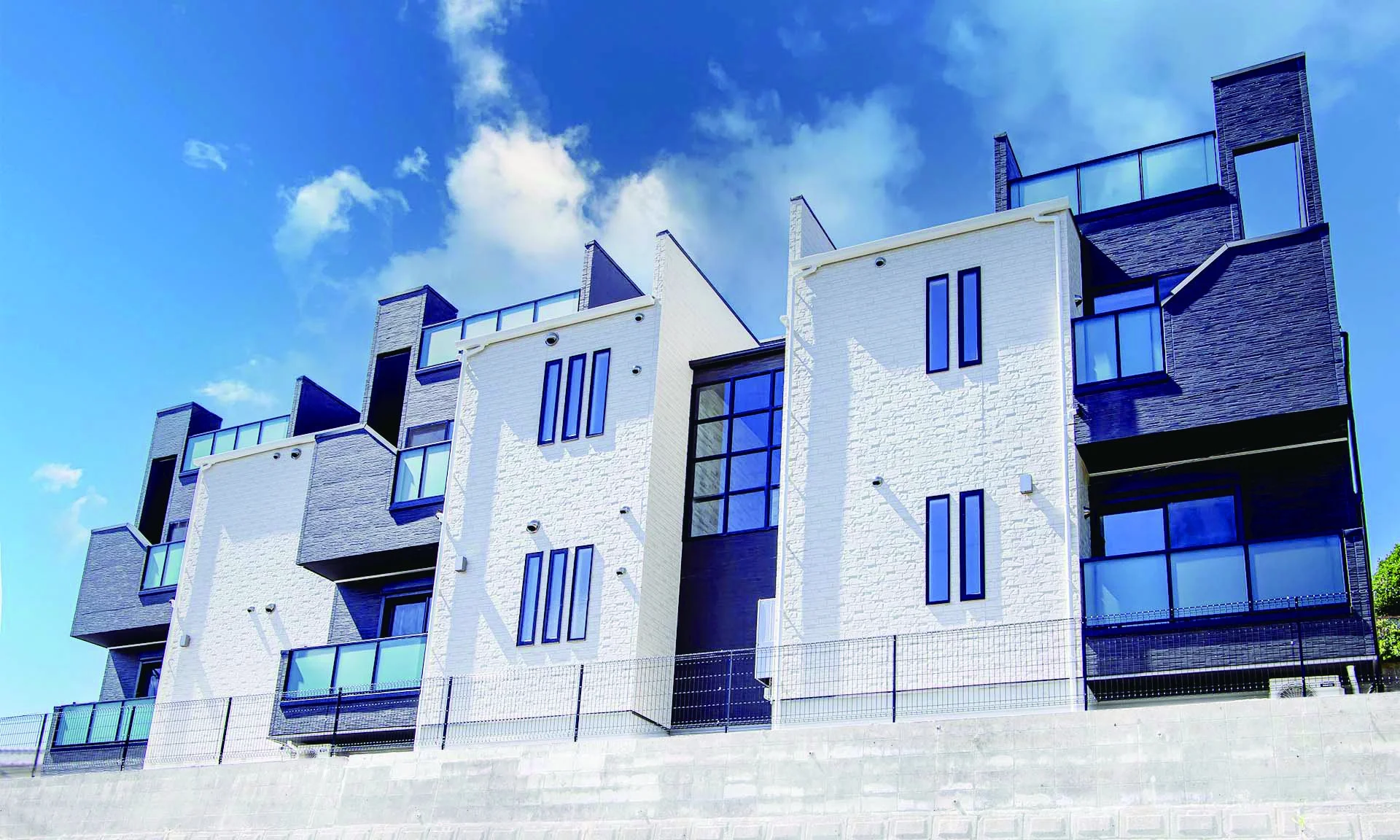 青空の下、白とダークグレーのコントラストが特徴的な現代的な集合住宅の外観