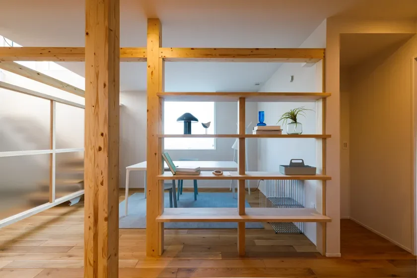 自然な木材の柱と棚が特徴的な、明るく開放感のあるモダンな室内空間です。ダイニングテーブルと椅子が見え、棚には植物やオブジェが飾られています。