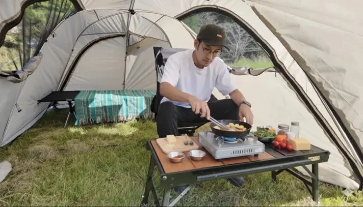 テントの中で男性がポータブルコンロを使って料理をしている様子
