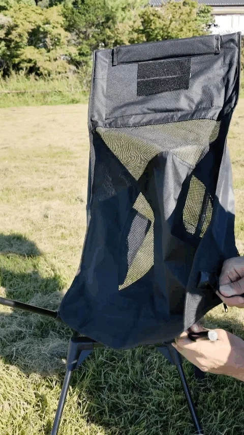 屋外の芝生の上で、黒いポータブルチェアを組み立てている様子